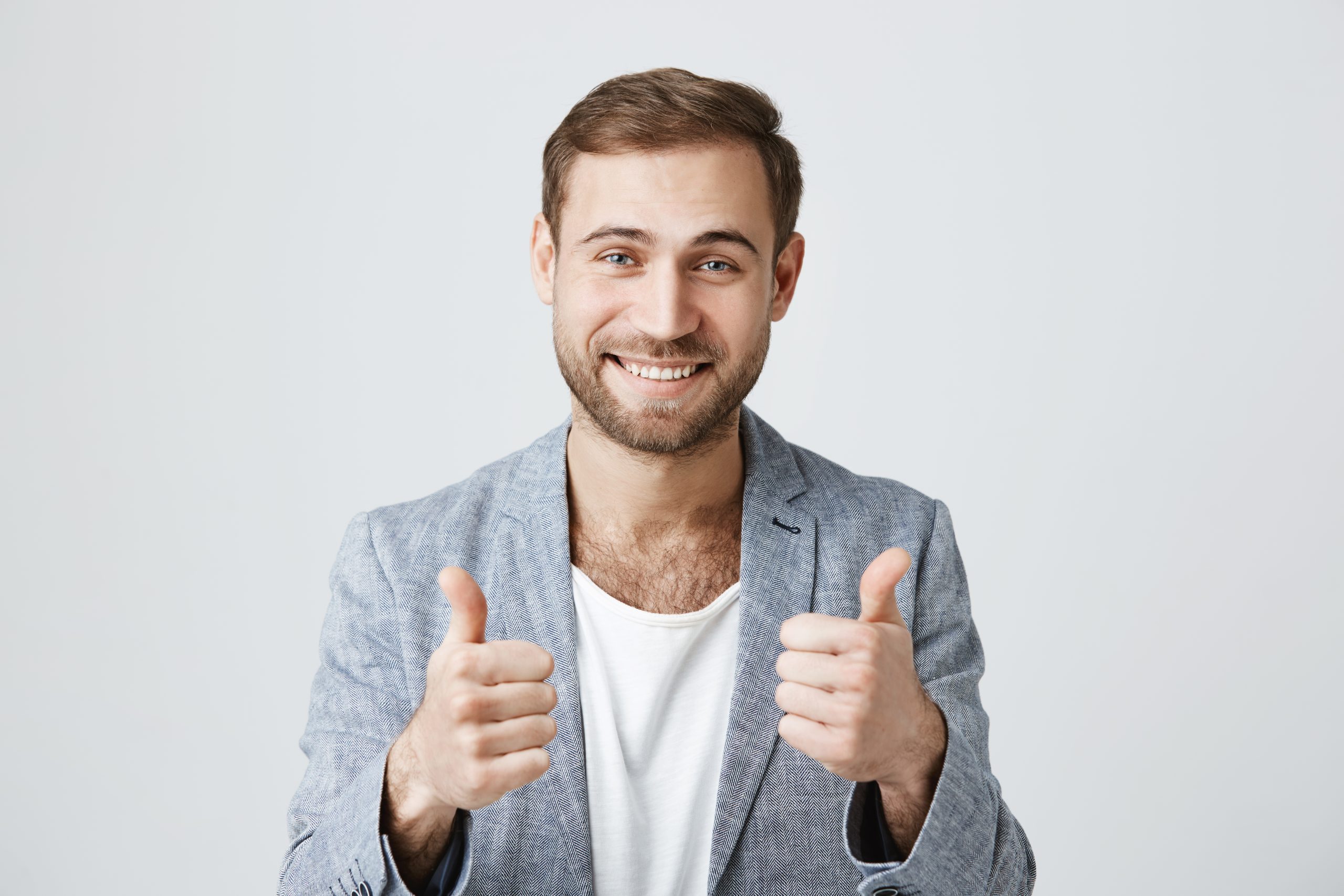 Portrait of stylish bearded man or customer with broad smile, looking at the camera with happy expression, showing thumbs-up with both hands, achieving professional goals. Body language